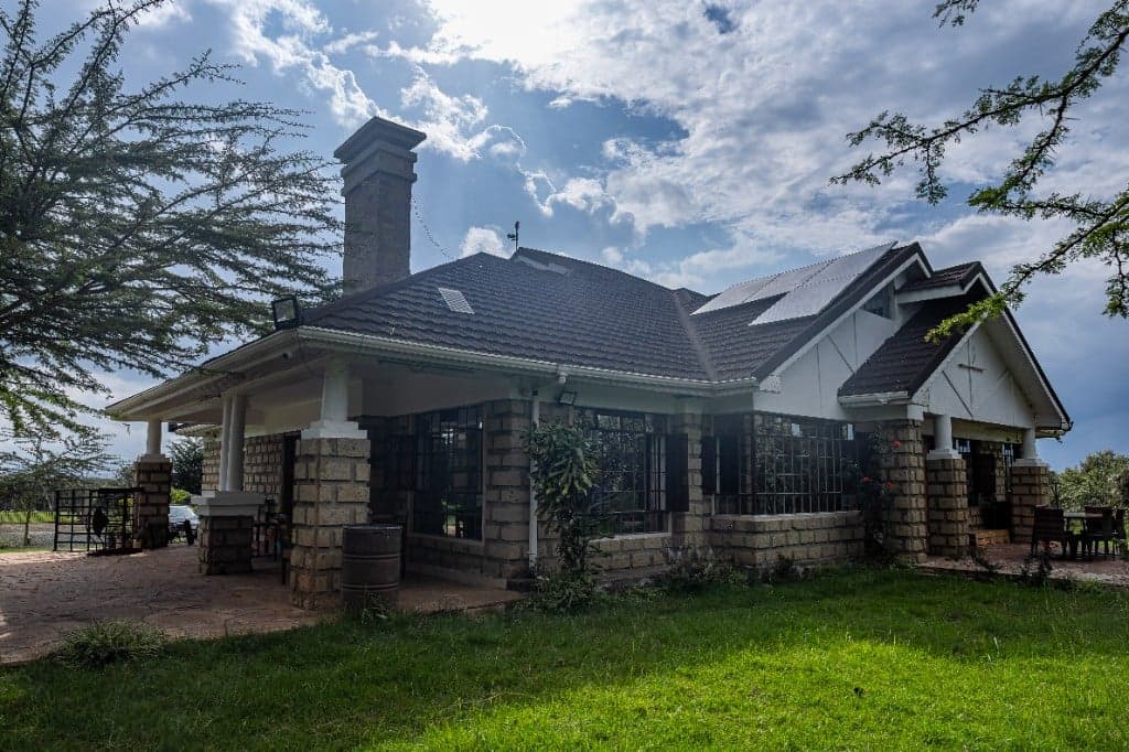 Whole House at Wadich — stone lodge with tiled roof, veranda, solar panels, and acacia trees